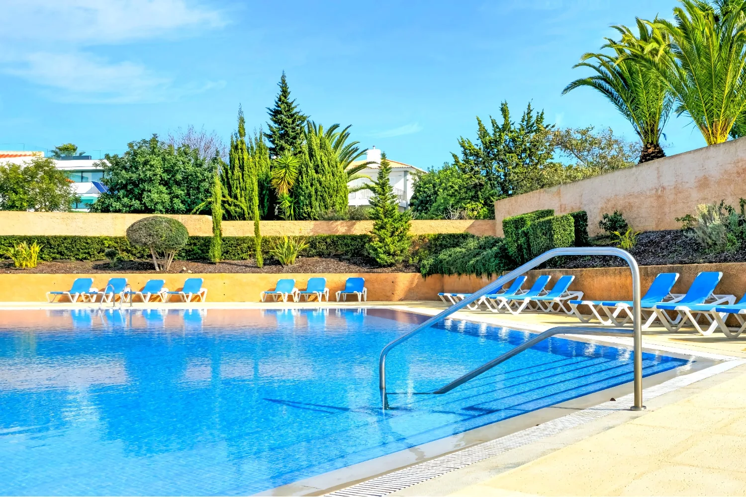 An outdoor swimming pool is surrounded by lounge seating and landscaped greenery.