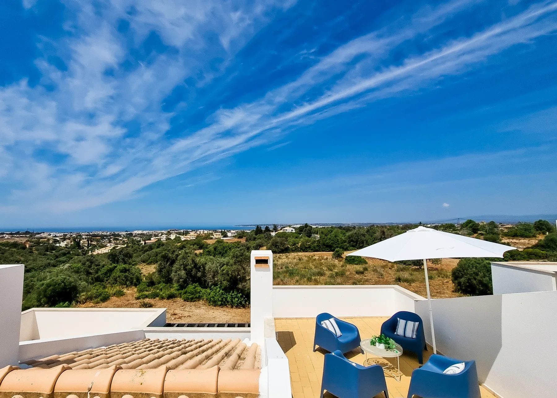 Una terraza en la azotea con asientos azules y un amplio paisaje costero al fondo.