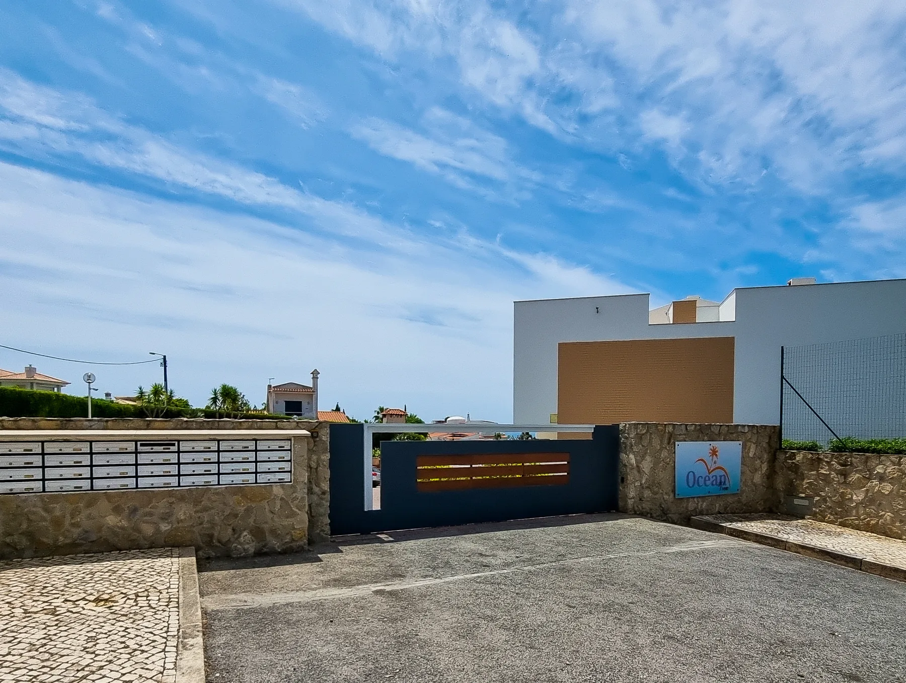 A paved entrance leads to a modern building behind a low stone wall.
