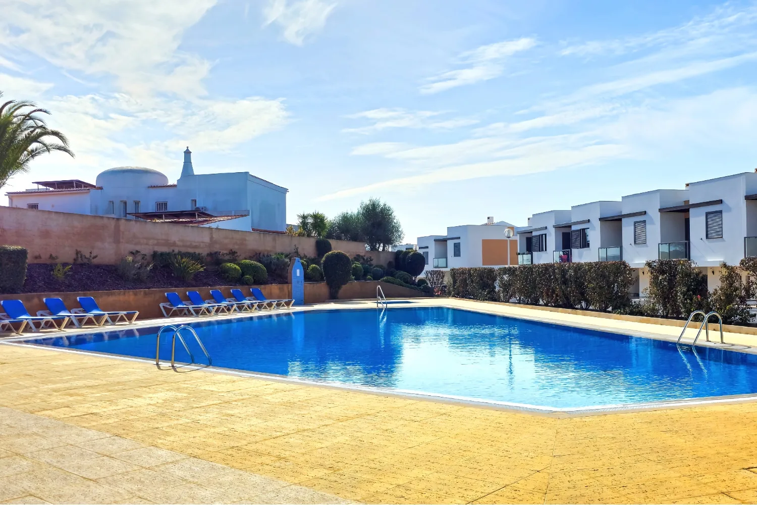 An outdoor swimming pool sits beside a paved deck and row of loungers.