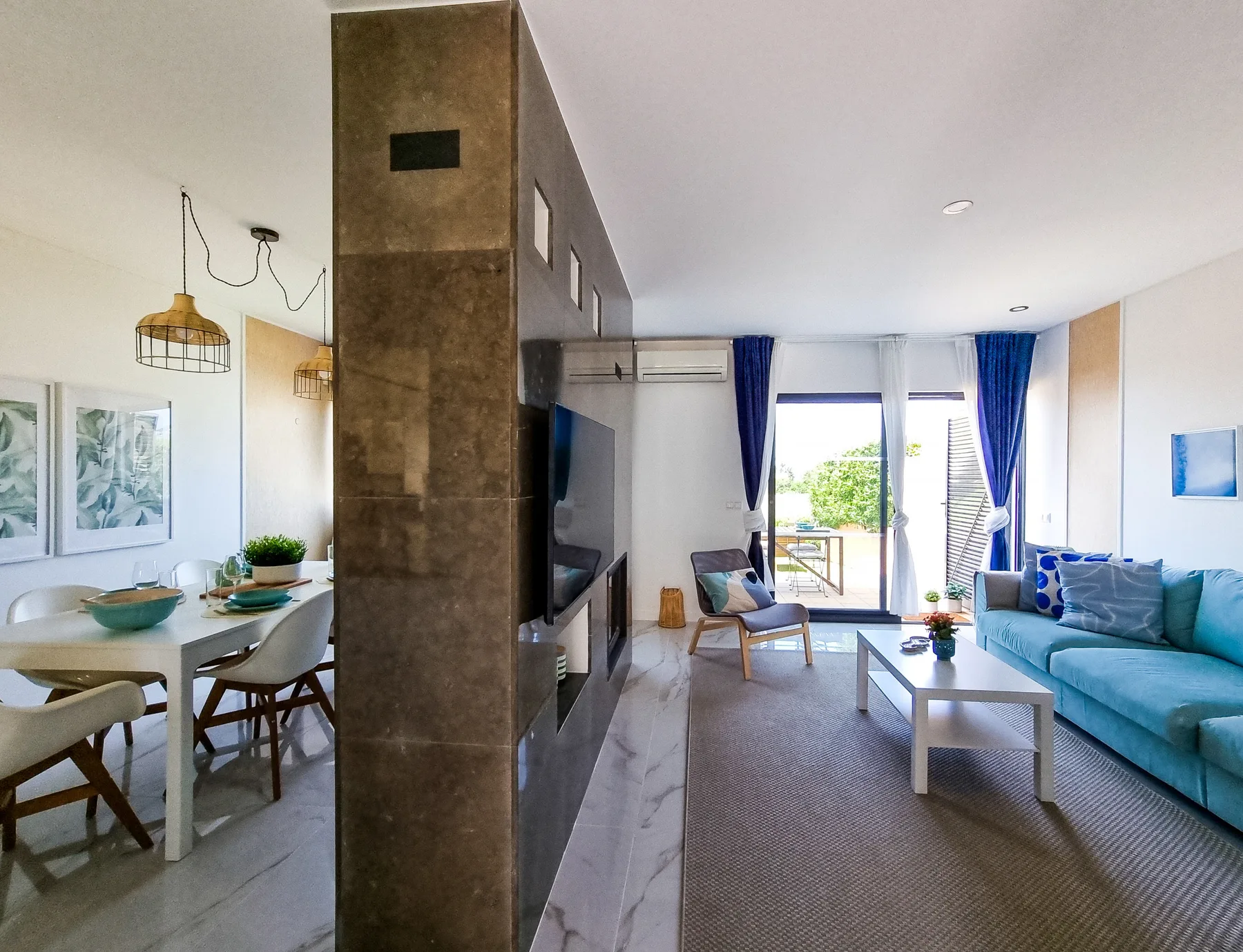Open-plan living and dining area with a blue sofa and large windows.