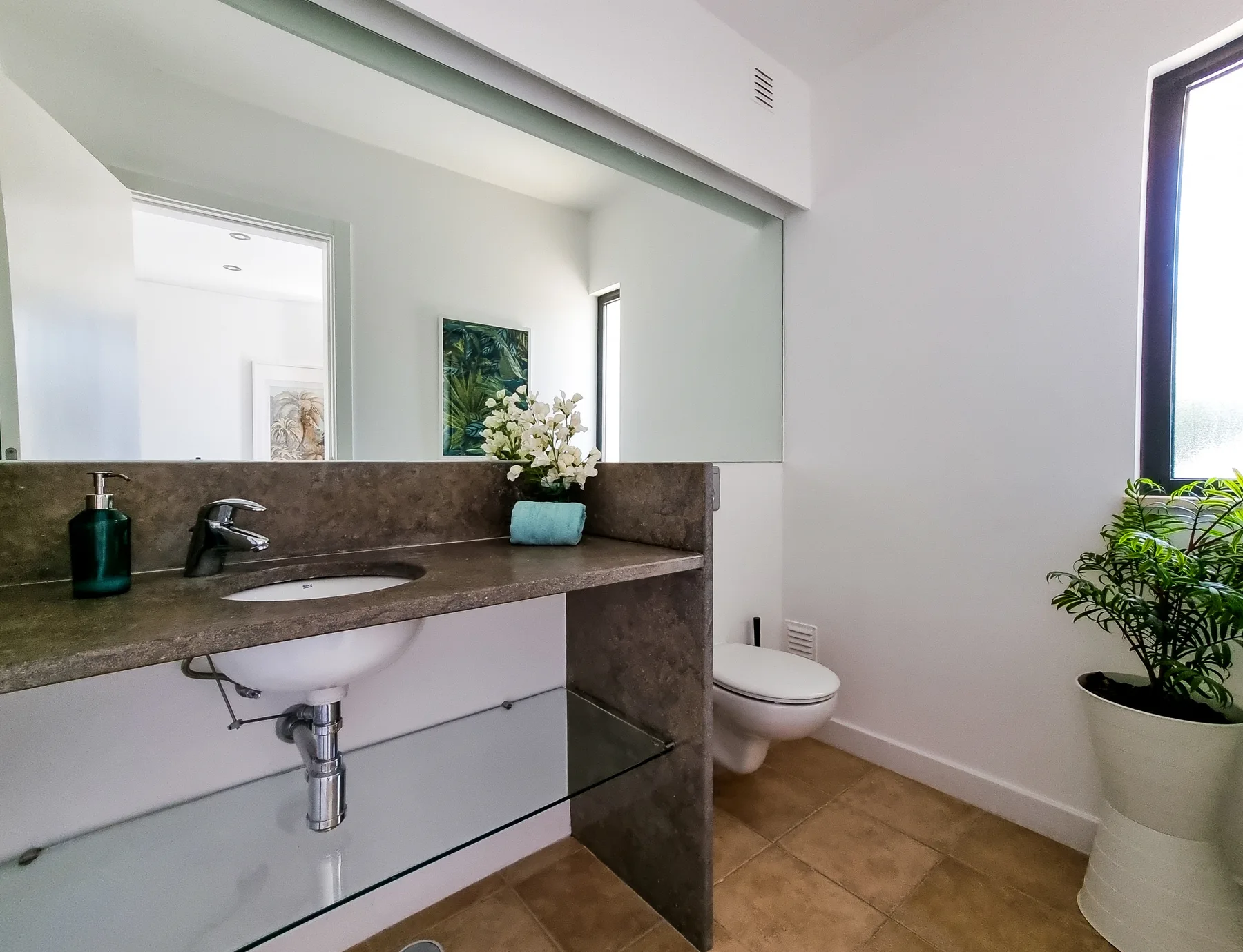 A bathroom with a sink, toilet, and potted plant beside the window.