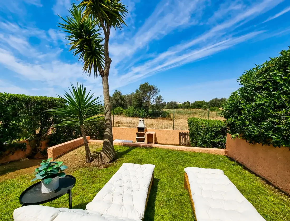 A garden seating area has two white loungers on the grass.
