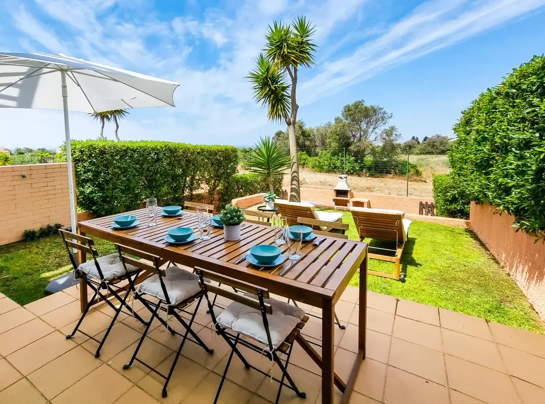 An outdoor dining patio with a table, chairs, and a green lawn.