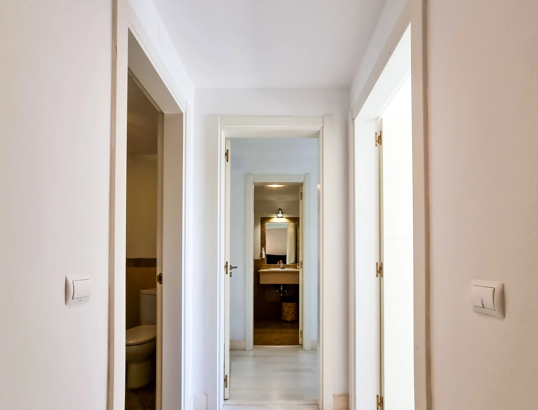 A bright hallway leads to a bathroom, with open doorways along the corridor.