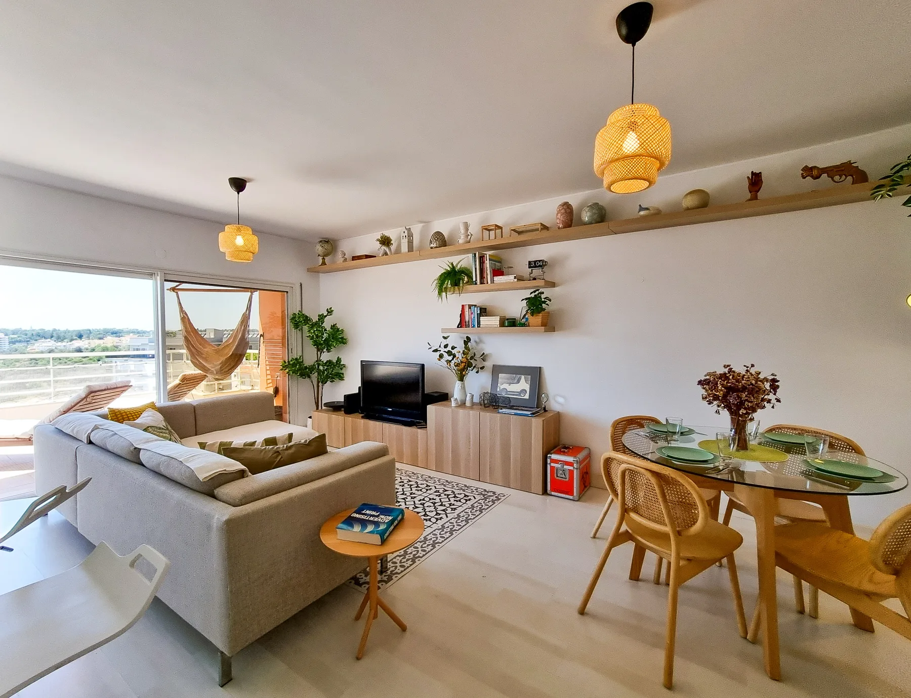 A bright living and dining room with seating, a television, and a glass dining table.