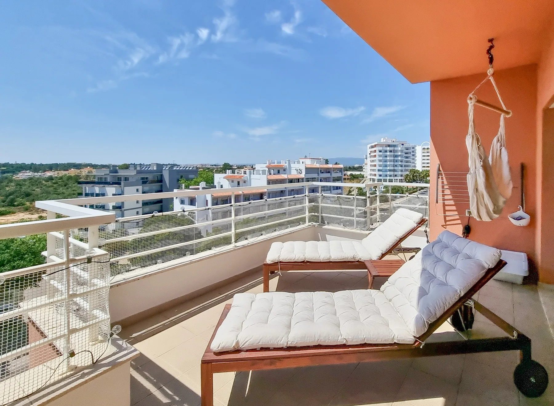 A sunny balcony with cushioned lounge seating and views of nearby buildings.