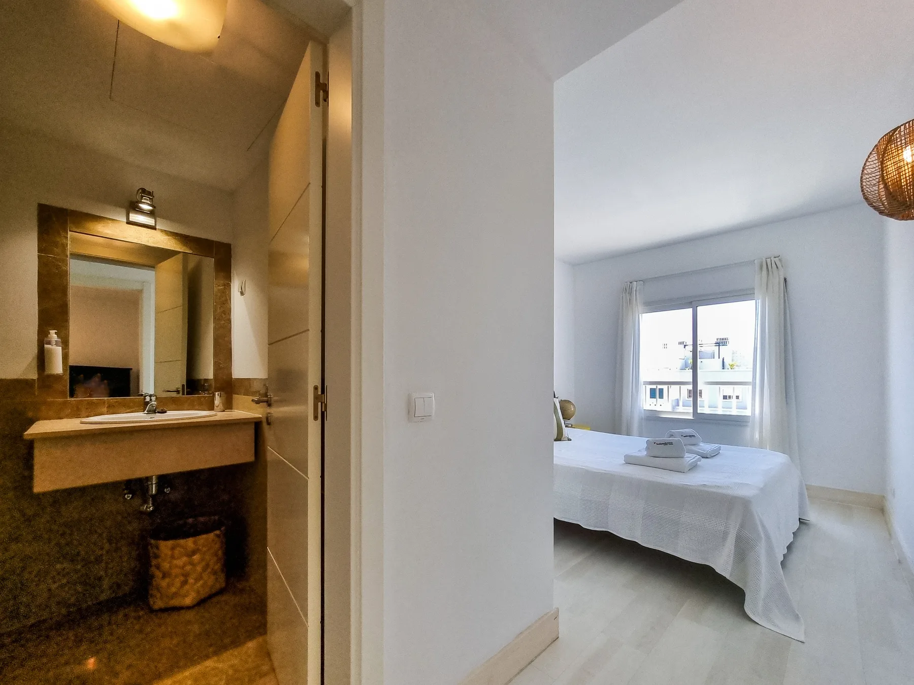 A bedroom with a neatly made bed and an adjoining bathroom vanity.
