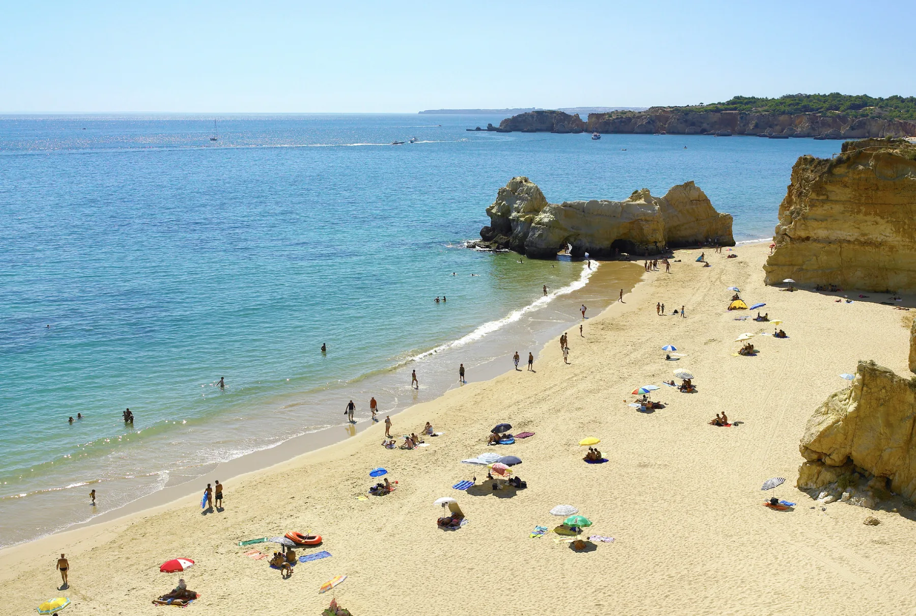 A sandy beach with swimmers in calm water beside rocky cliffs.