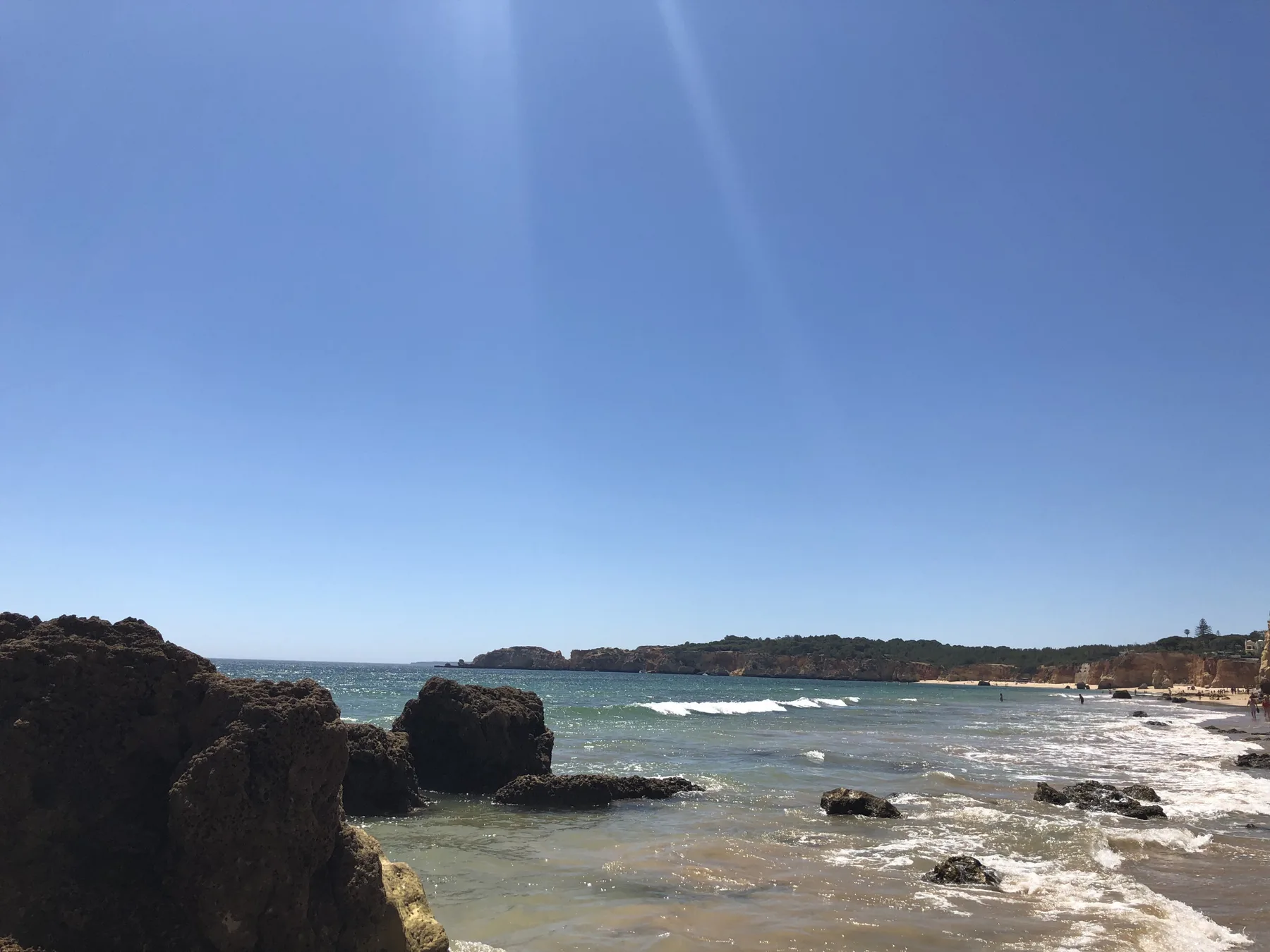 A rocky shoreline borders the sea beneath a clear blue sky.
