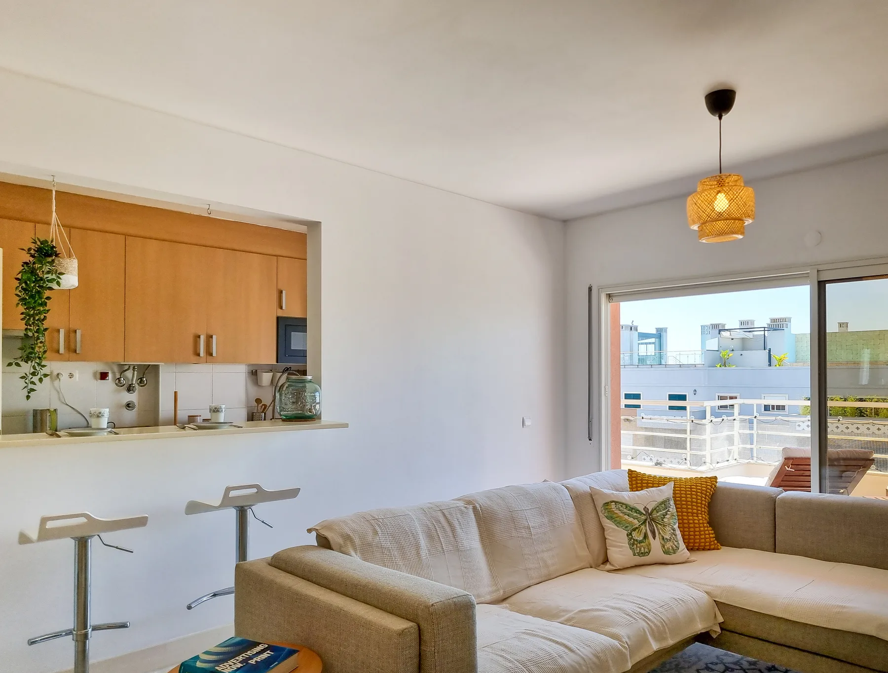 Living room with a sectional seating area beside an open kitchen and balcony.