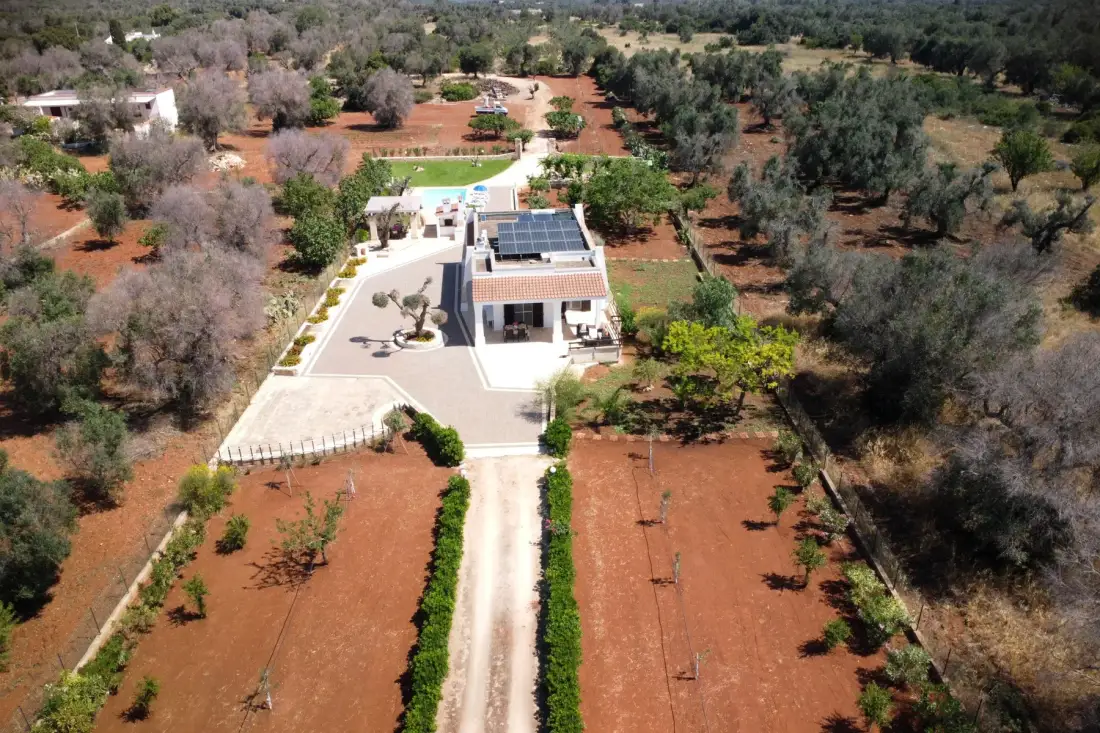 Aerial view of a modern house with a driveway amid red-earth fields and trees.