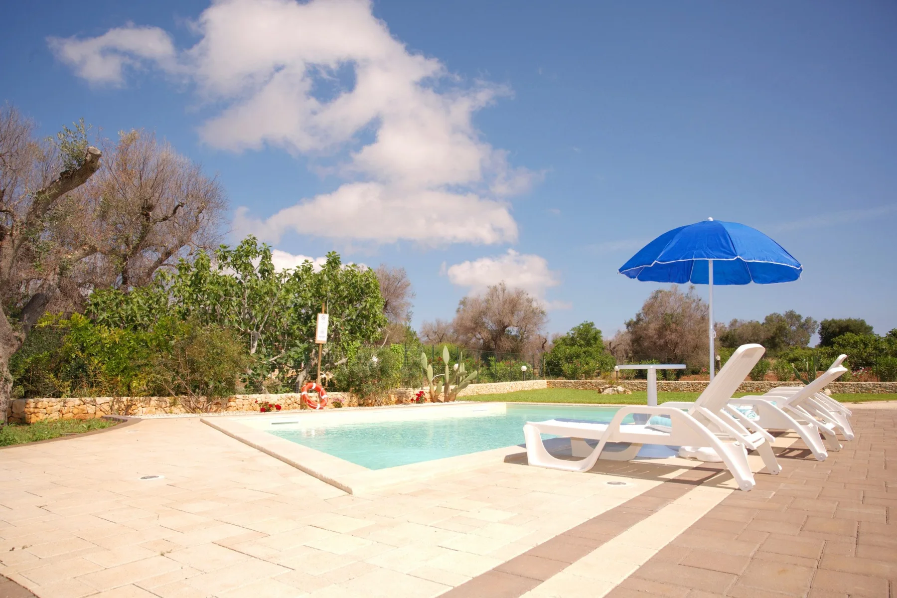 An outdoor swimming pool is surrounded by a paved deck and lounge seating.
