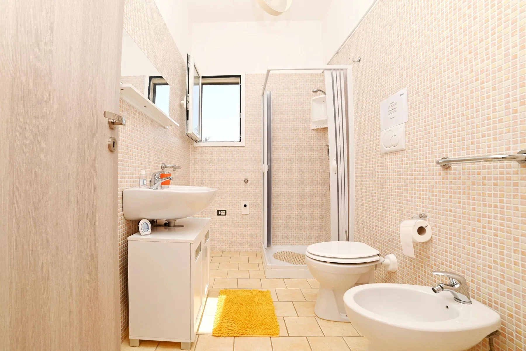 A bright tiled bathroom with a sink, toilet, and shower.