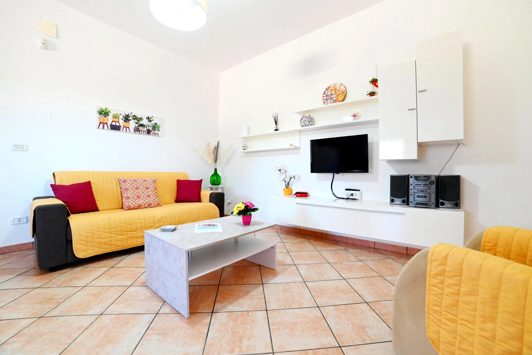 A bright living room with a yellow sofa and a television on the wall.