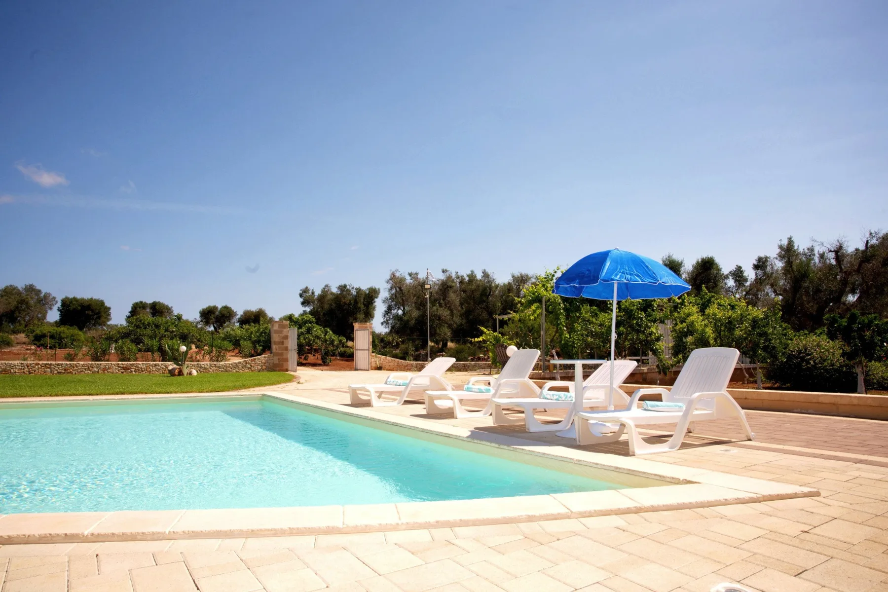 An outdoor swimming pool with lounge seating and a blue umbrella beside it.
