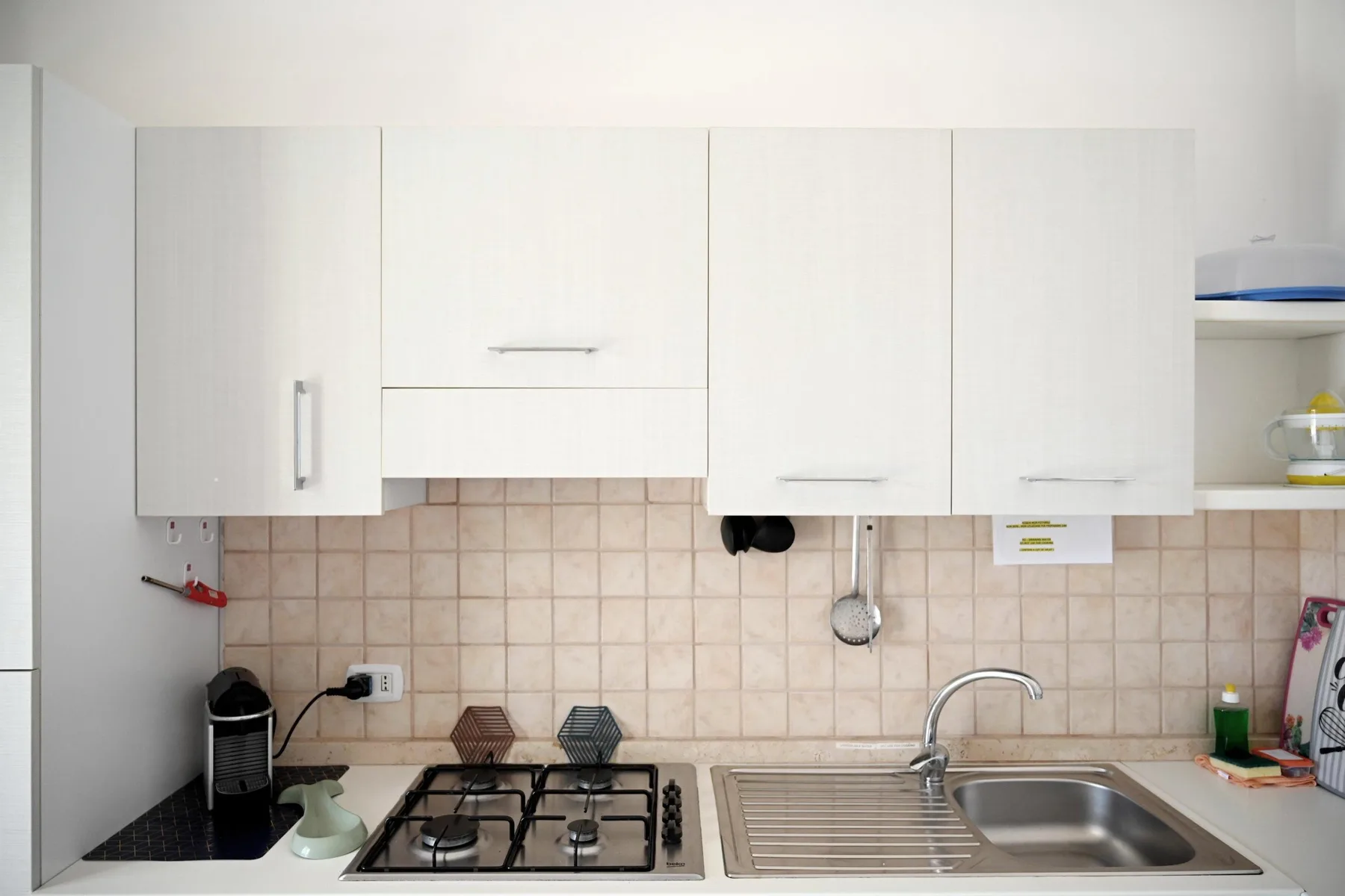 A kitchen counter with a gas cooktop, sink, and white cabinets.
