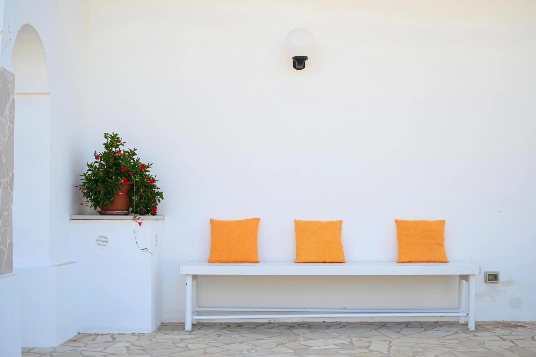A white outdoor seating area features a long bench with orange cushions.