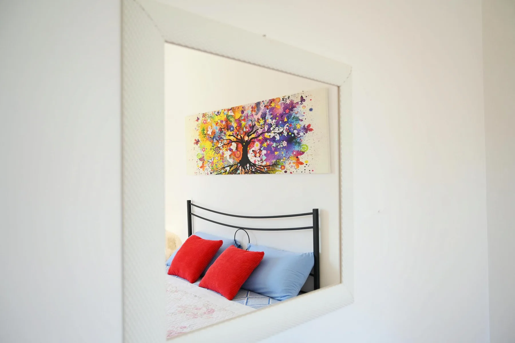 A bed with colorful tree artwork hanging above it.