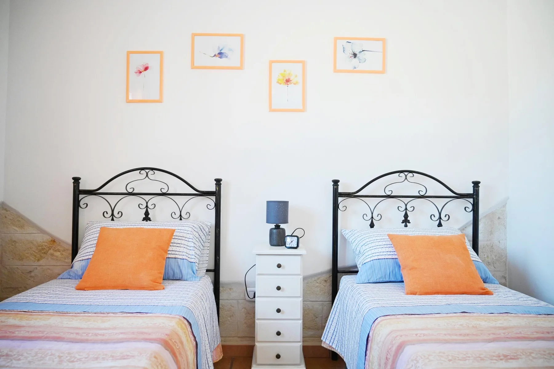 A bedroom with two single beds, a small bedside table, and framed artwork.