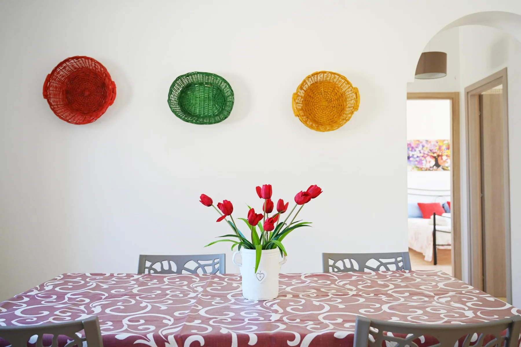 A dining area with a patterned tablecloth and red flowers in a vase.