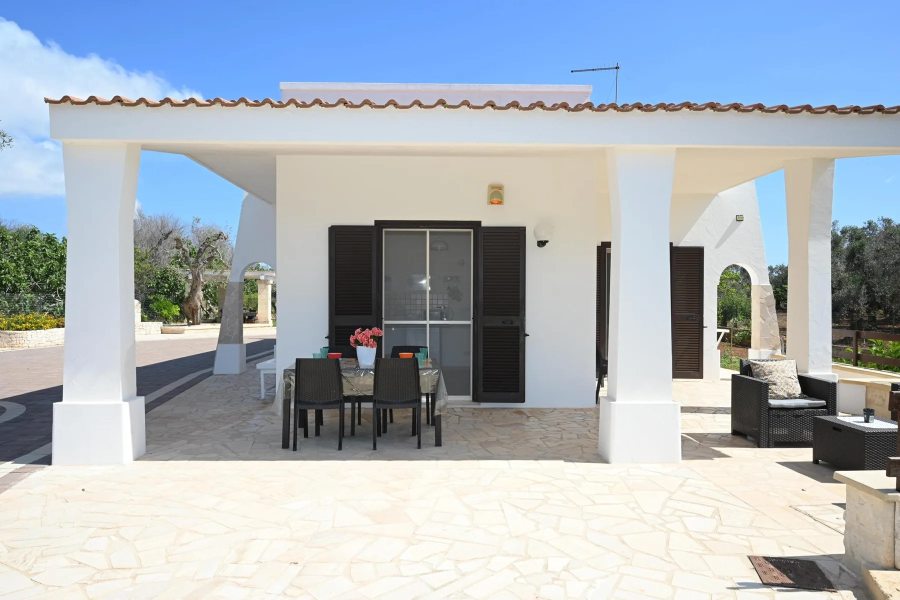 A white outdoor patio with a dining table and seating beside the house.