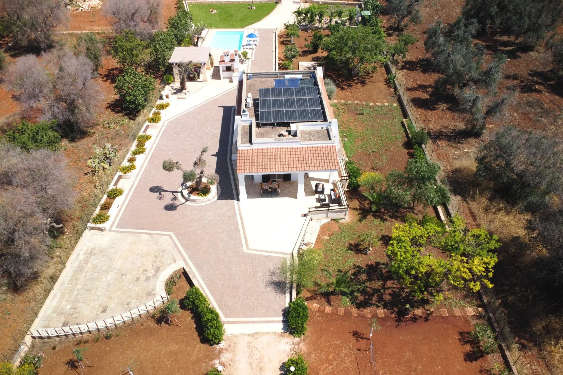 An aerial view shows a house, paved driveway, swimming pool, and surrounding trees.