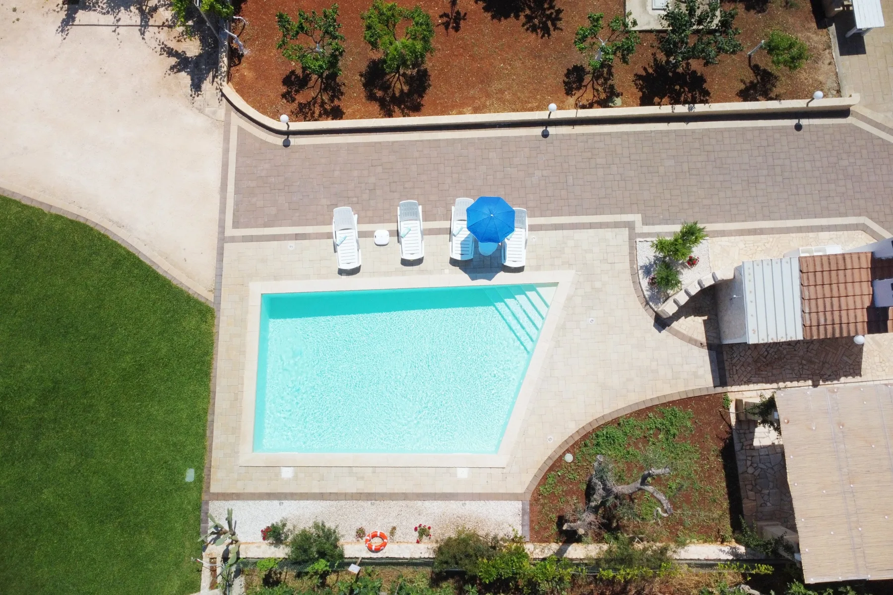 An outdoor swimming pool sits beside a paved patio with lounge seating.