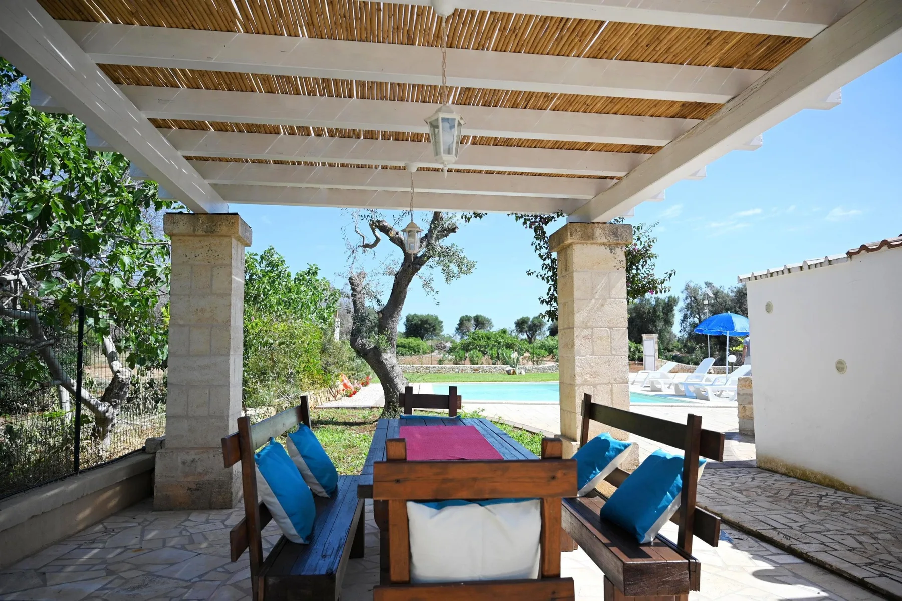 A shaded outdoor dining area under a pergola overlooks a swimming pool.