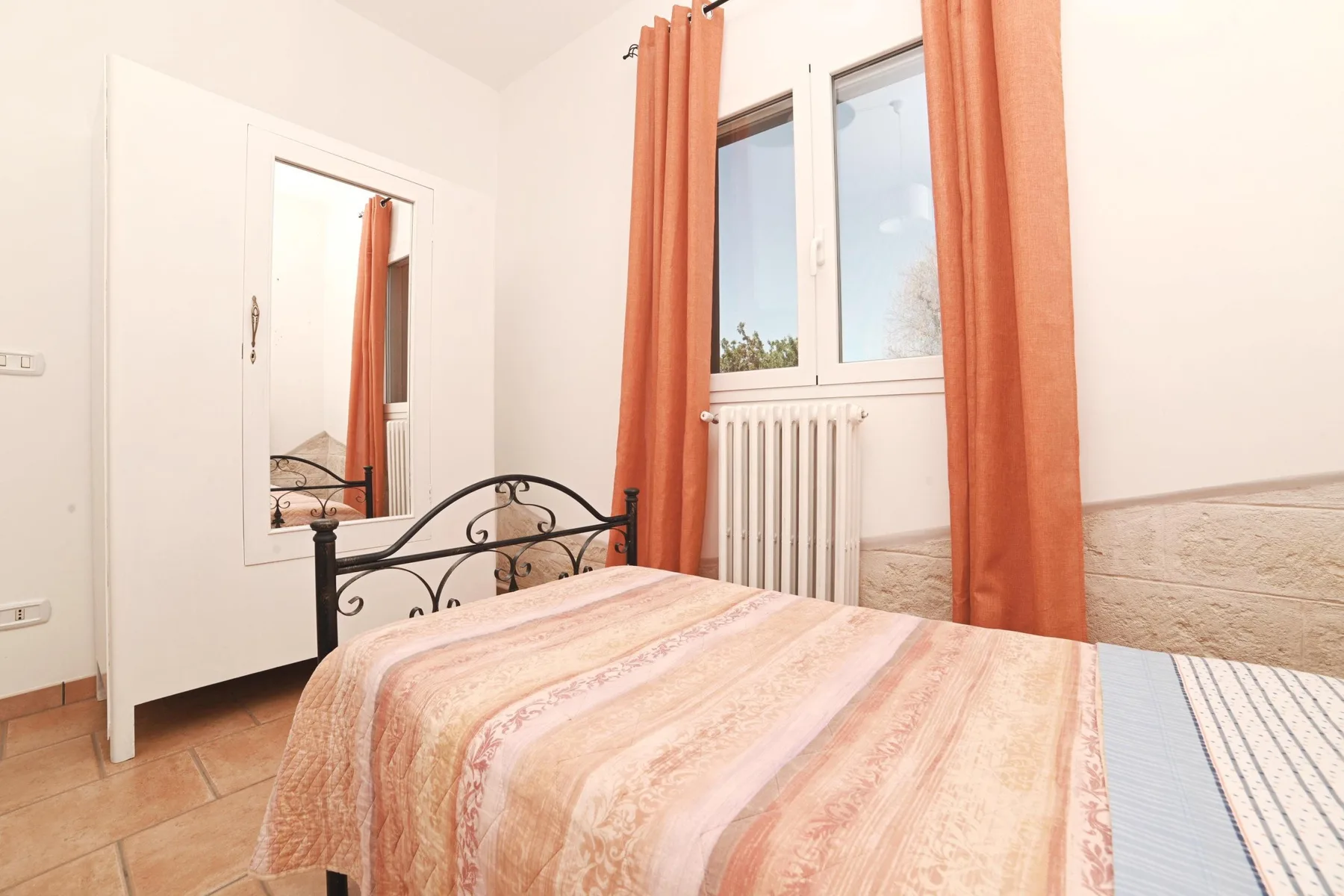 A bedroom with a bed, window, and orange curtains.