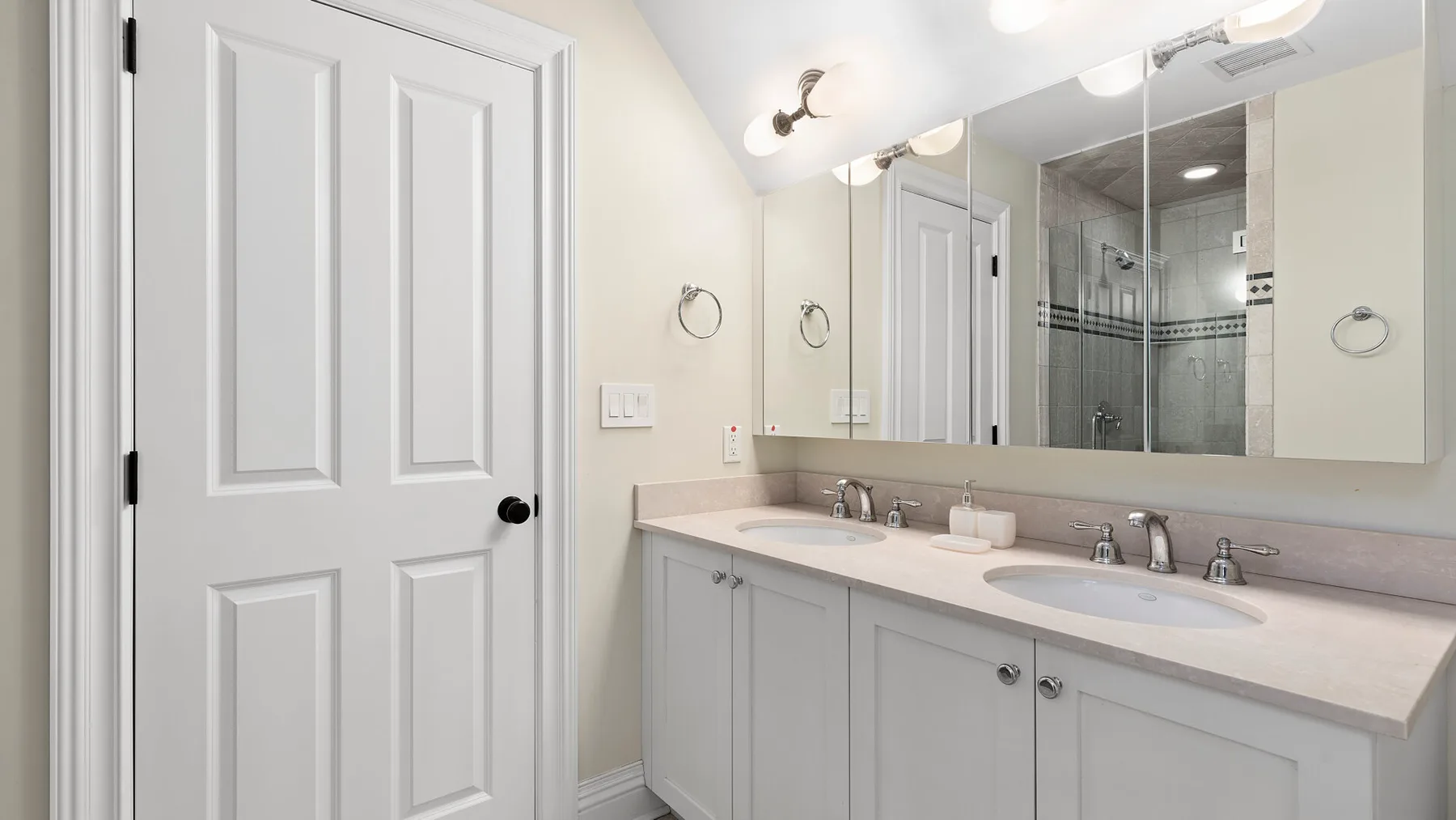 Un baño luminoso con un tocador largo y una ducha con mampara de vidrio.