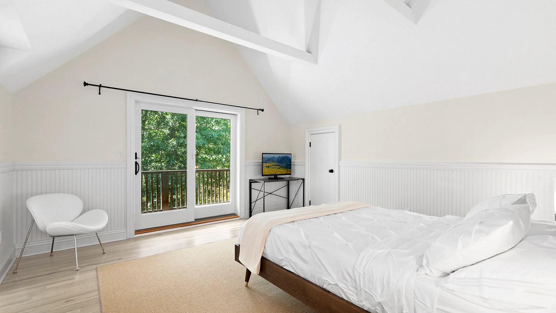 Dormitorio con una cama, puertas corredizas de vidrio y una pequeña zona para sentarse.