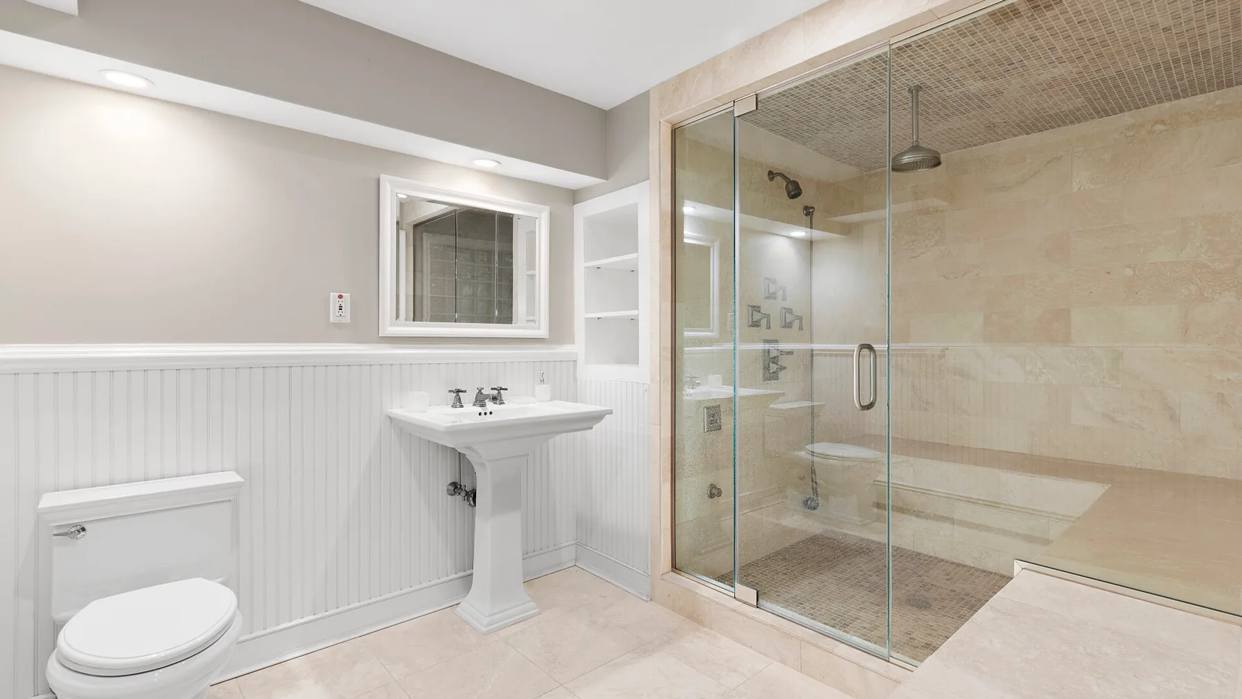 Un baño luminoso con lavabo de pedestal, inodoro y ducha con mampara de vidrio.