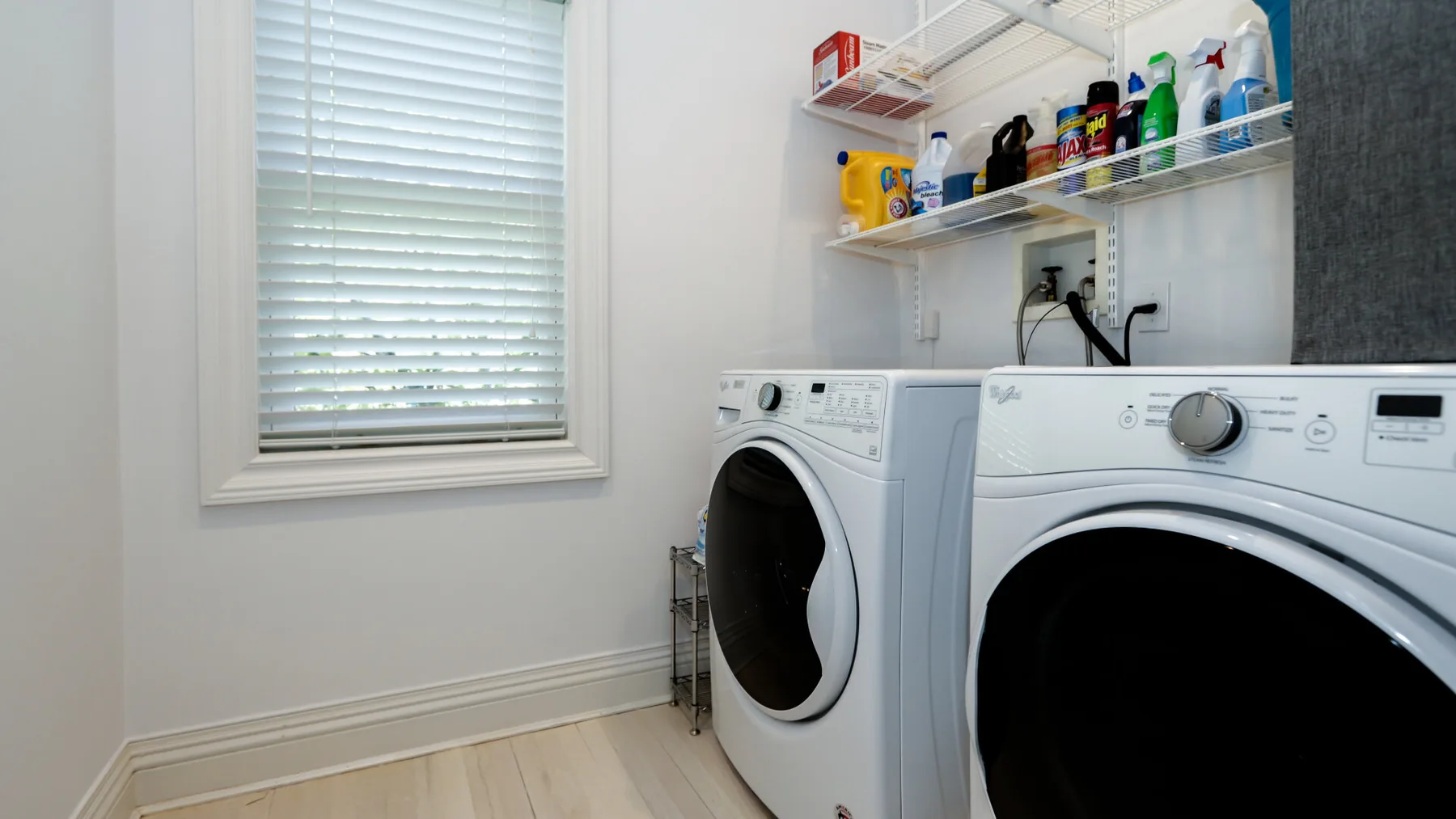 Un cuarto de lavandería con dos máquinas de carga frontal y estantes con productos de limpieza.