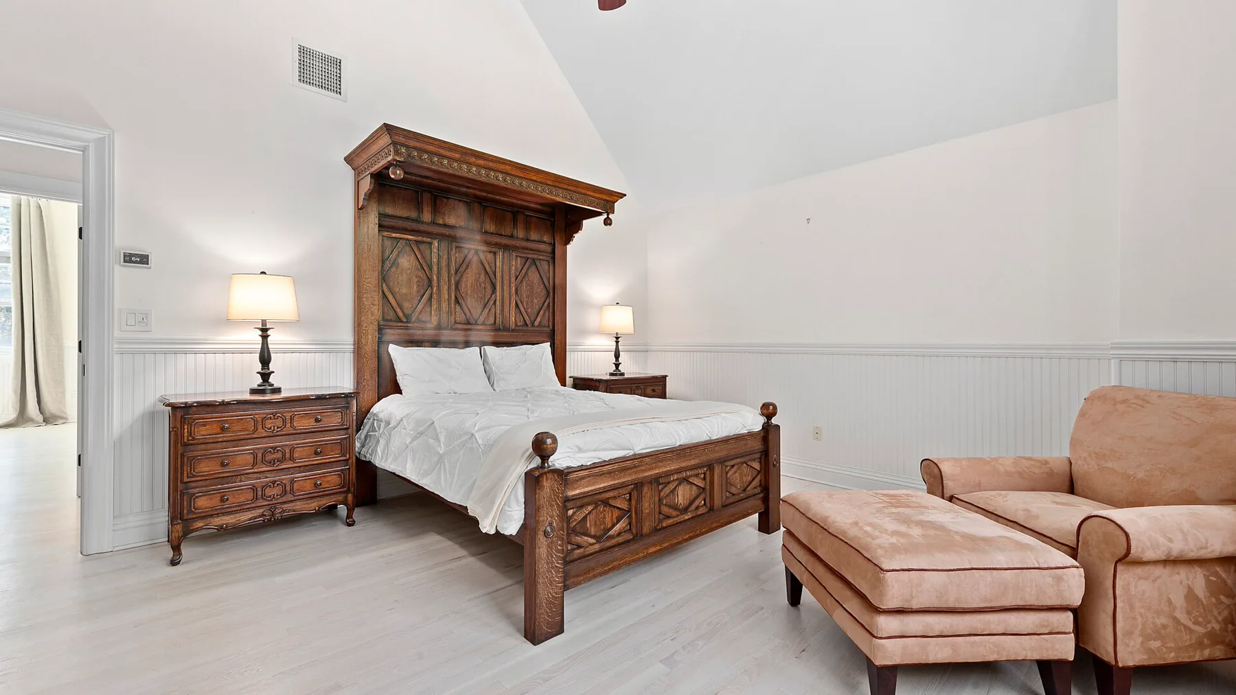 Un dormitorio con una cama de madera tallada y una chaise longue color melocotón.