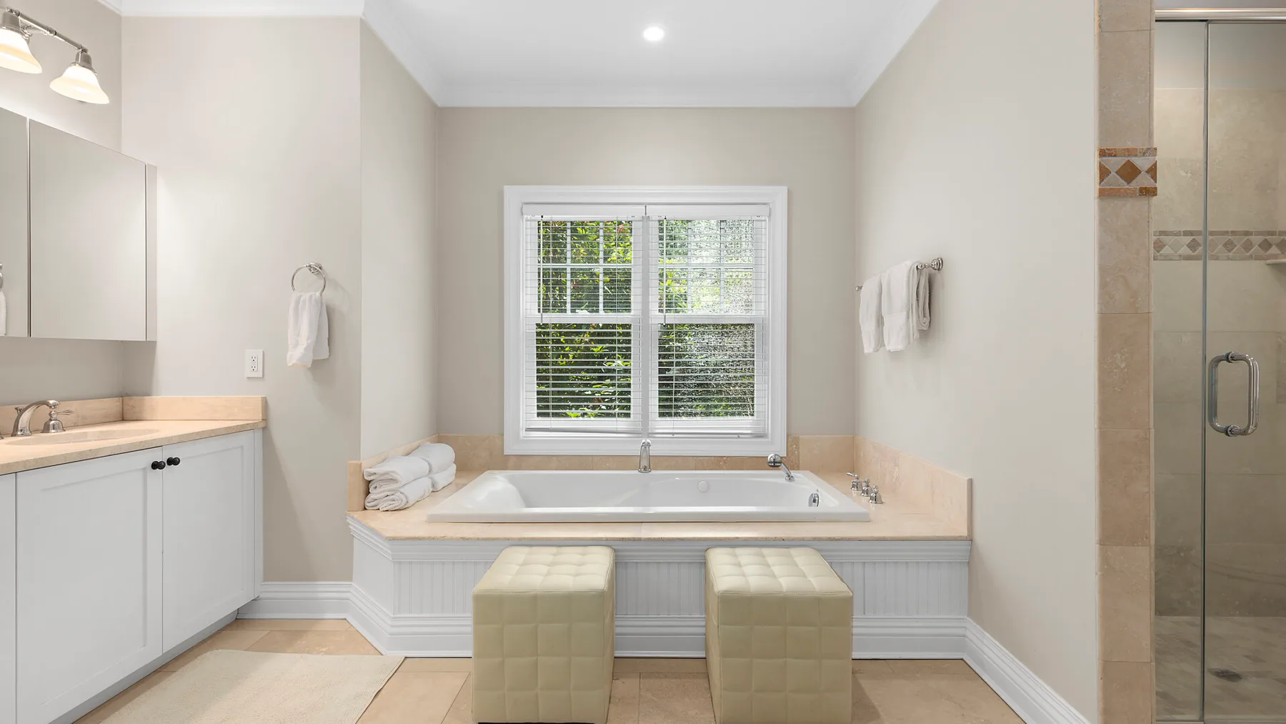 Un baño luminoso cuenta con una bañera bajo una ventana y una ducha de vidrio.