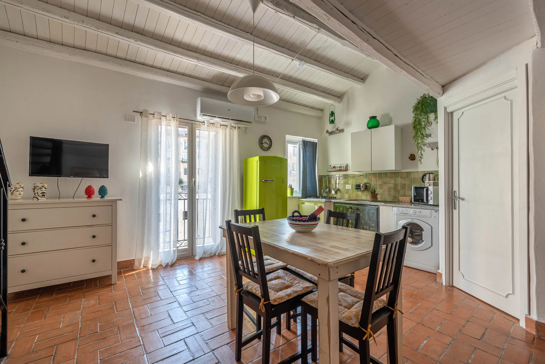 Una cocina y comedor con una mesa de madera, un refrigerador verde y piso de baldosas.