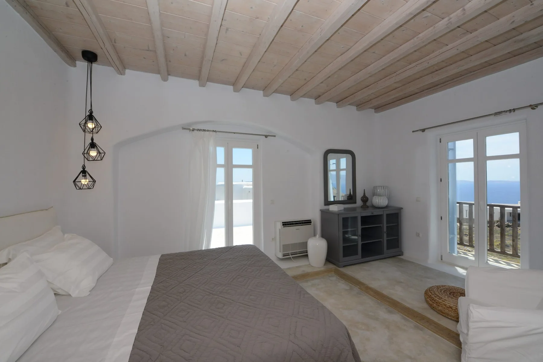 A bedroom with a bed, a low cabinet, and doors opening onto a sea view.