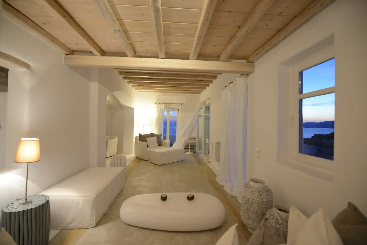 A bright living room with white seating and exposed wooden ceiling beams.
