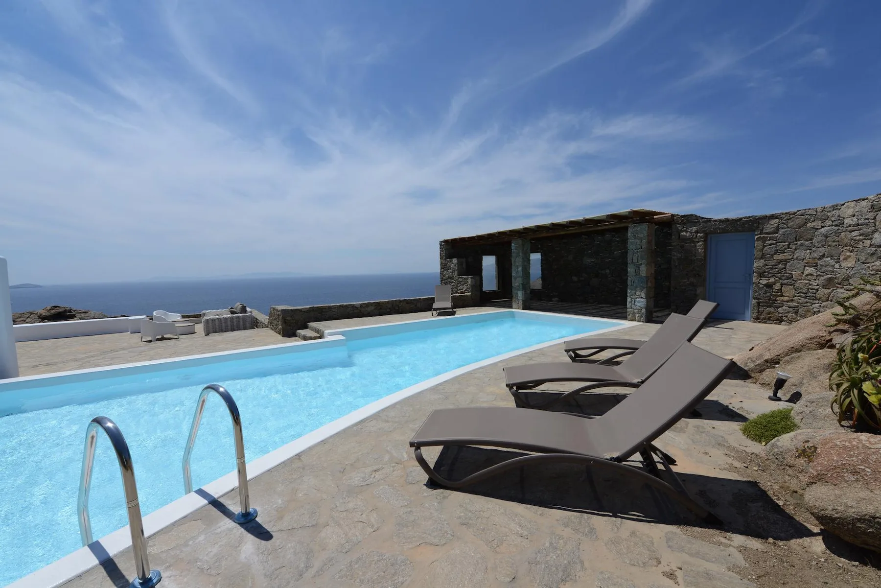 An outdoor swimming pool overlooks the sea, with loungers beside the water.
