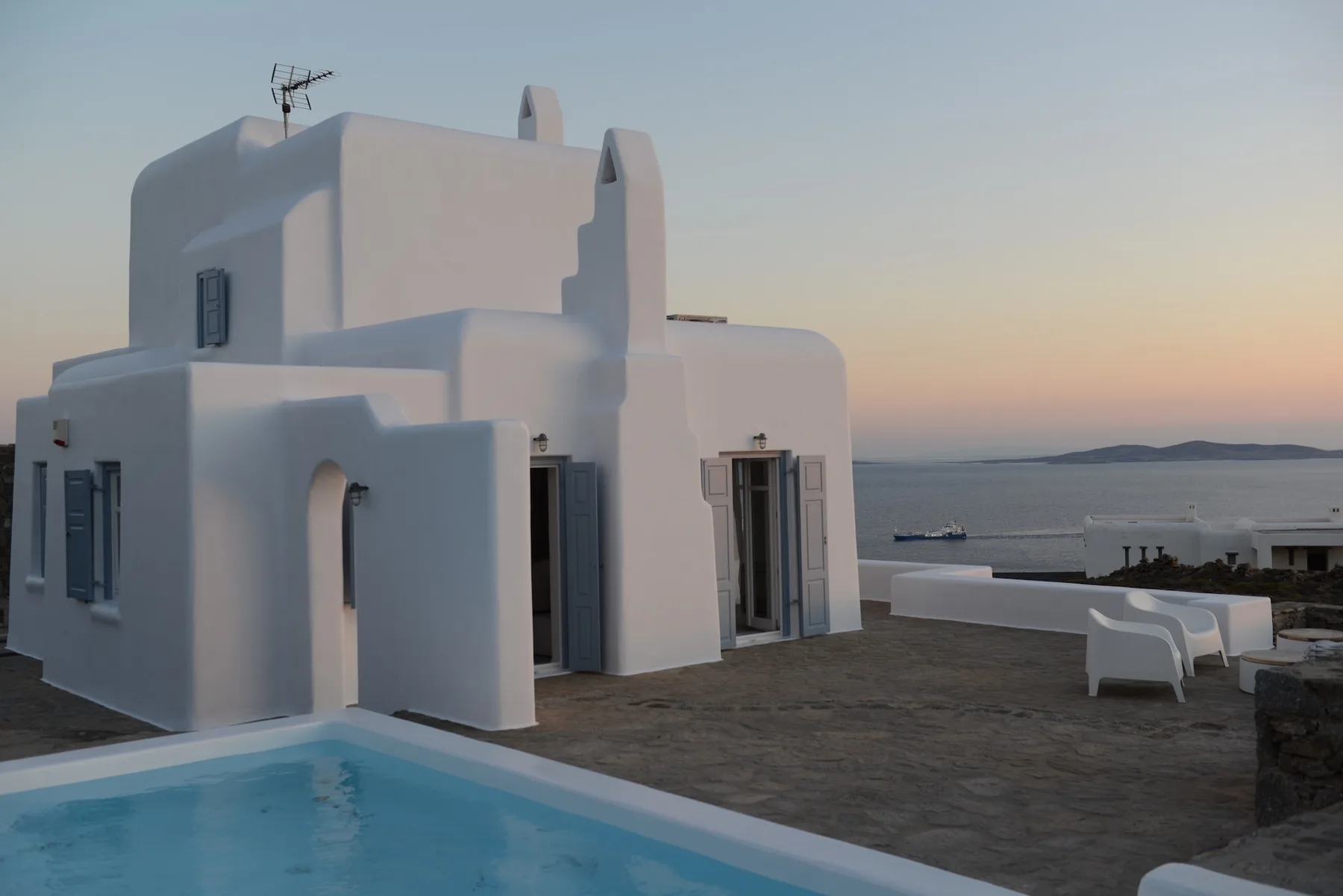 A white seaside house beside a swimming pool, with the sea visible beyond.