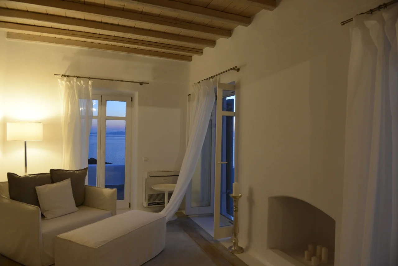 A living room with seating, an open glass door, and a view of the sea.