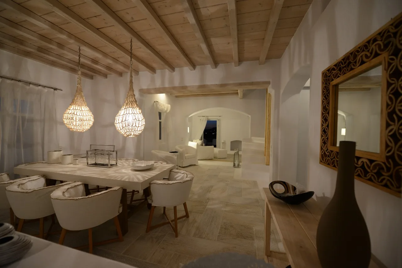 A dining and living area with a table beneath hanging lights and seating beyond.