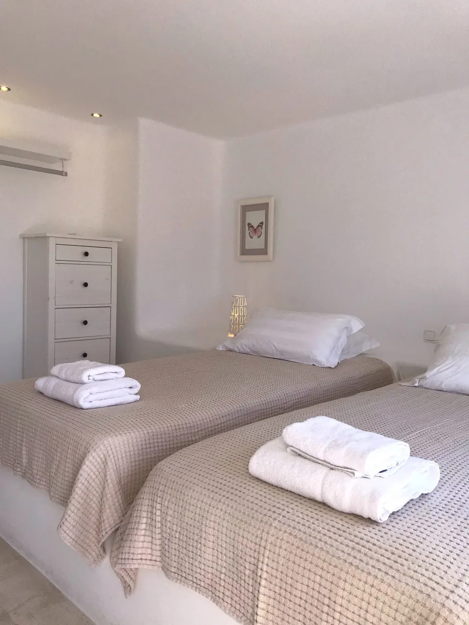 A bright bedroom with two beds and neatly folded white towels.