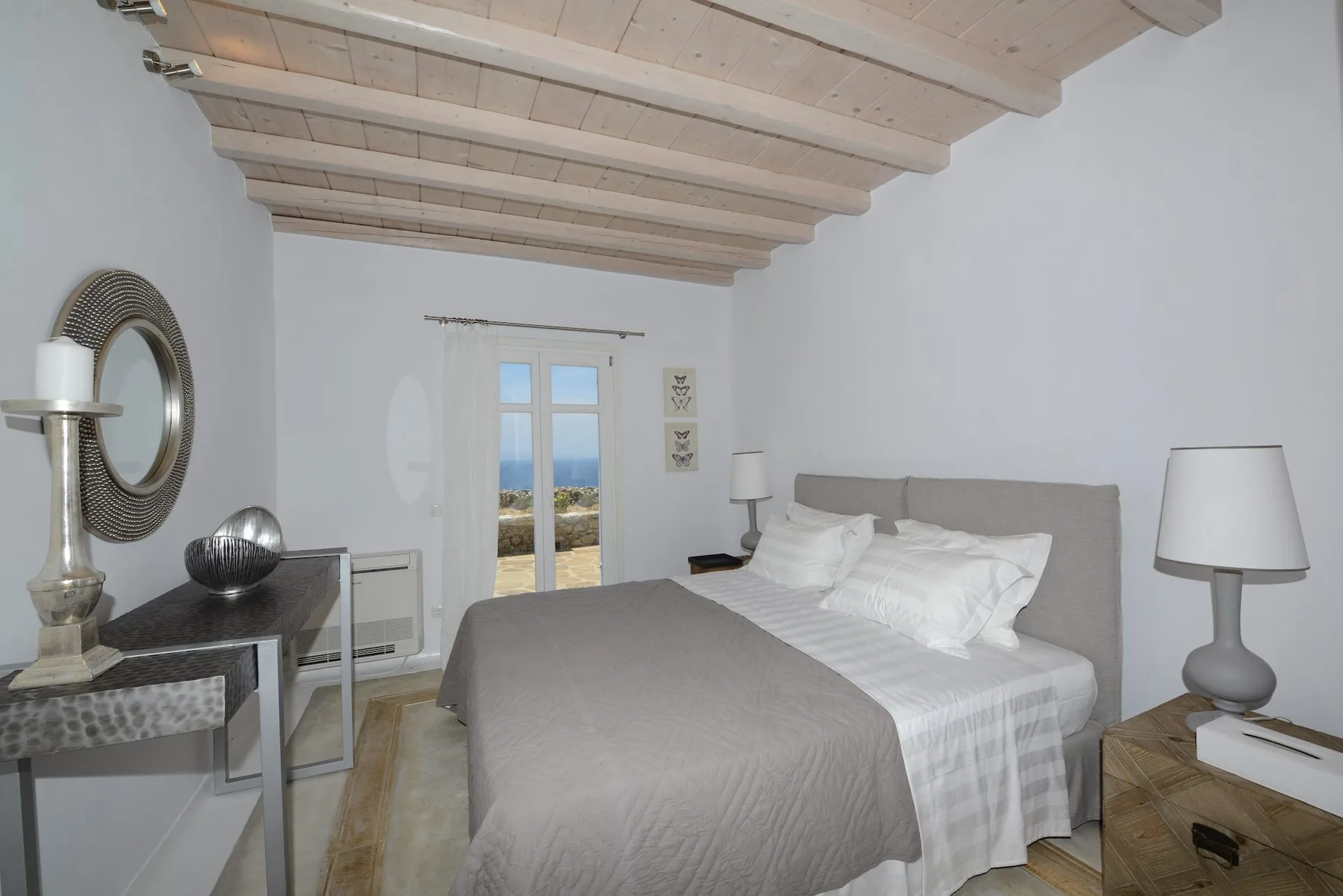 A bedroom with a neatly made bed, bedside lamps, and glass doors overlooking the sea.