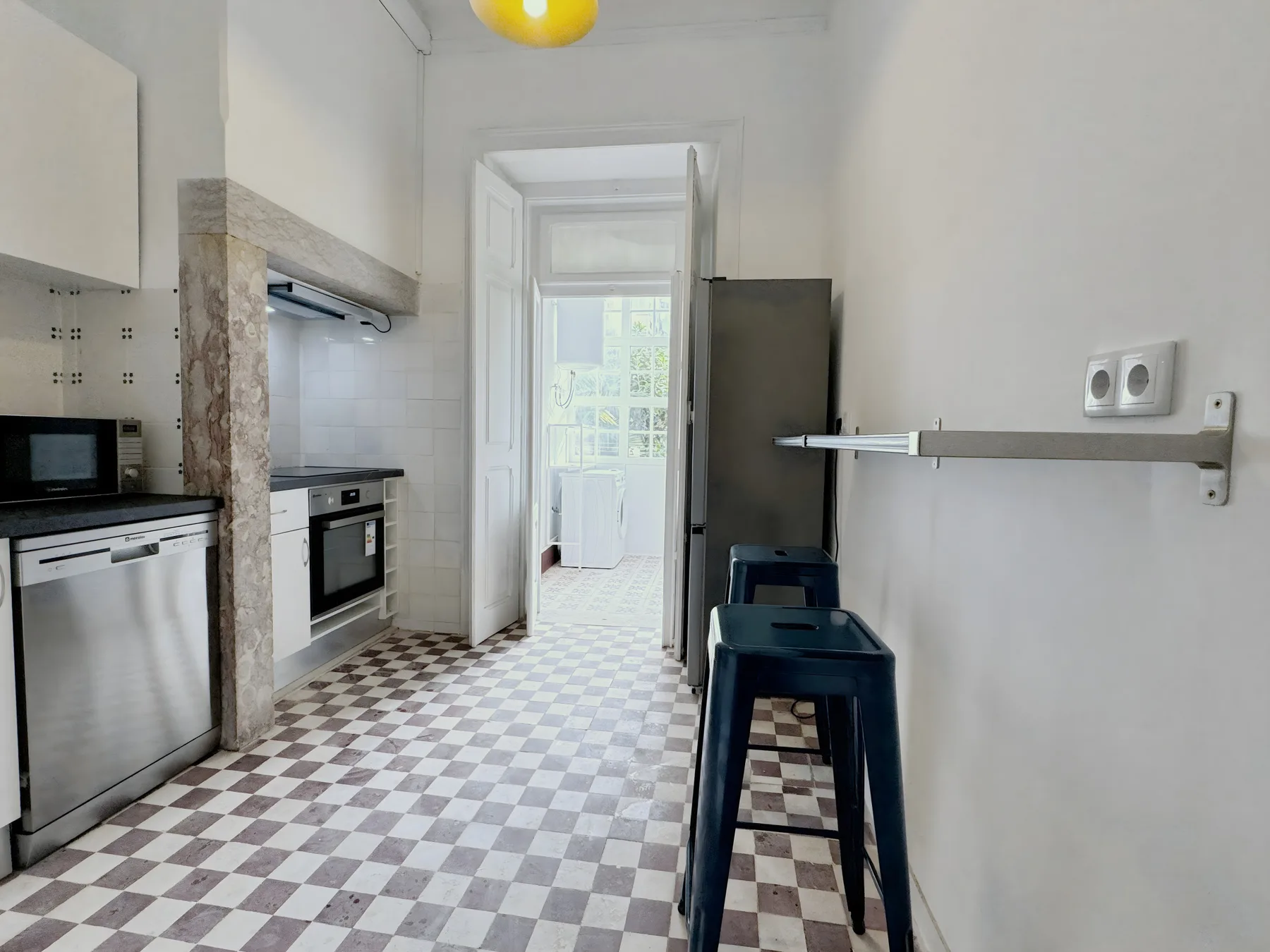 A narrow kitchen with a checkered floor and dark seating along the wall.