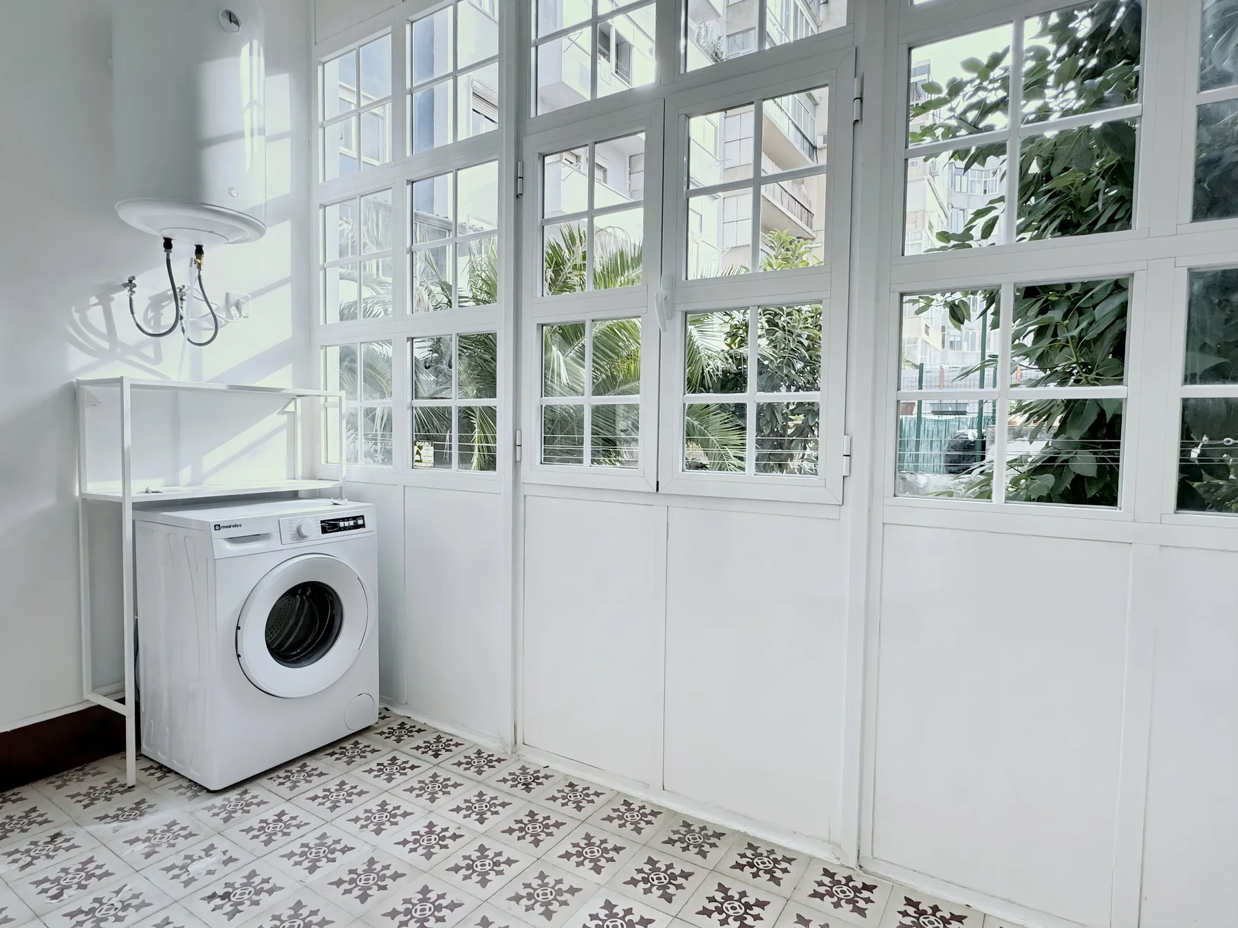A bright laundry room with a washing machine beside large grid windows.