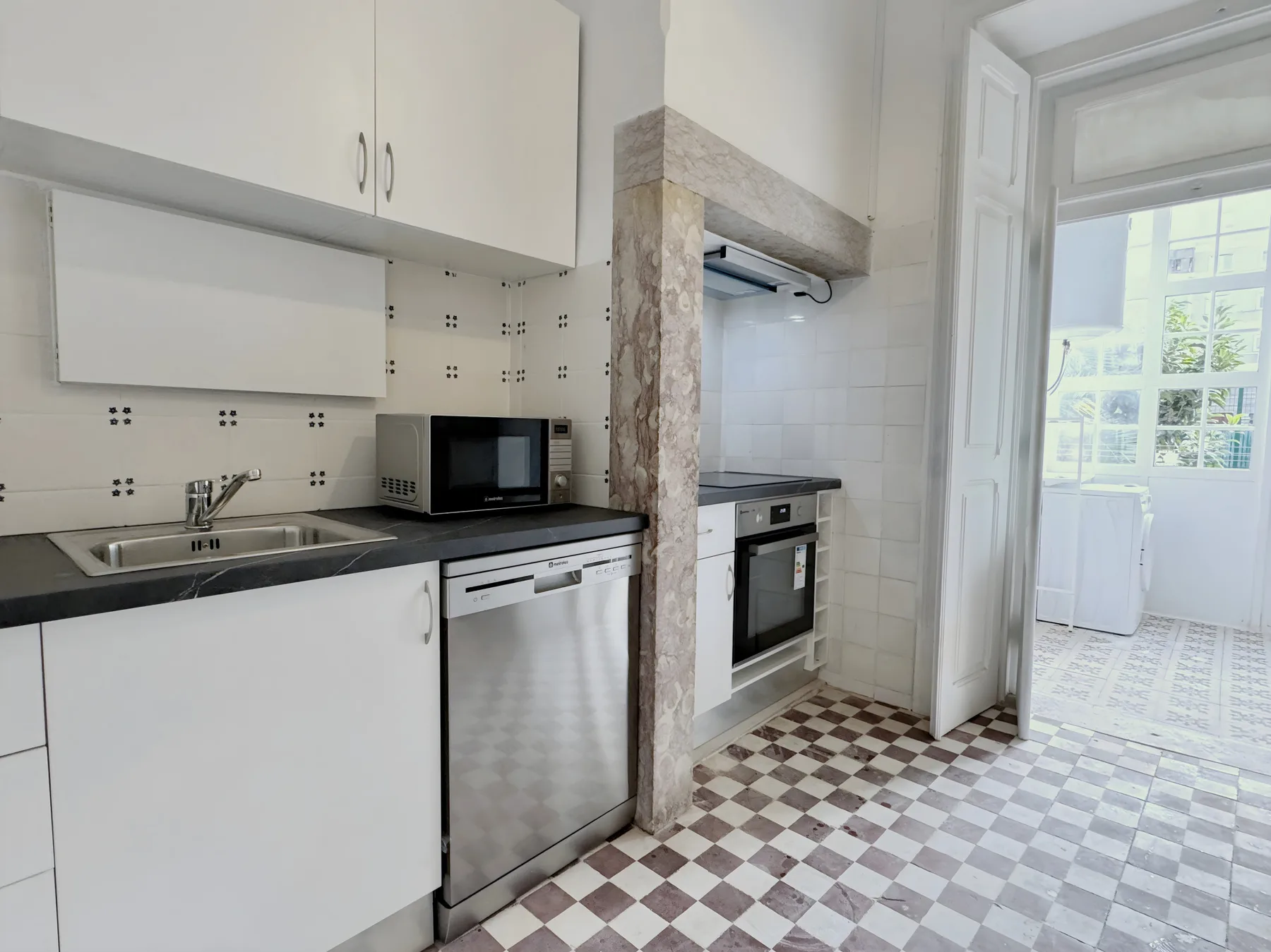 A bright kitchen with white cabinets, a countertop, and a checkered floor.