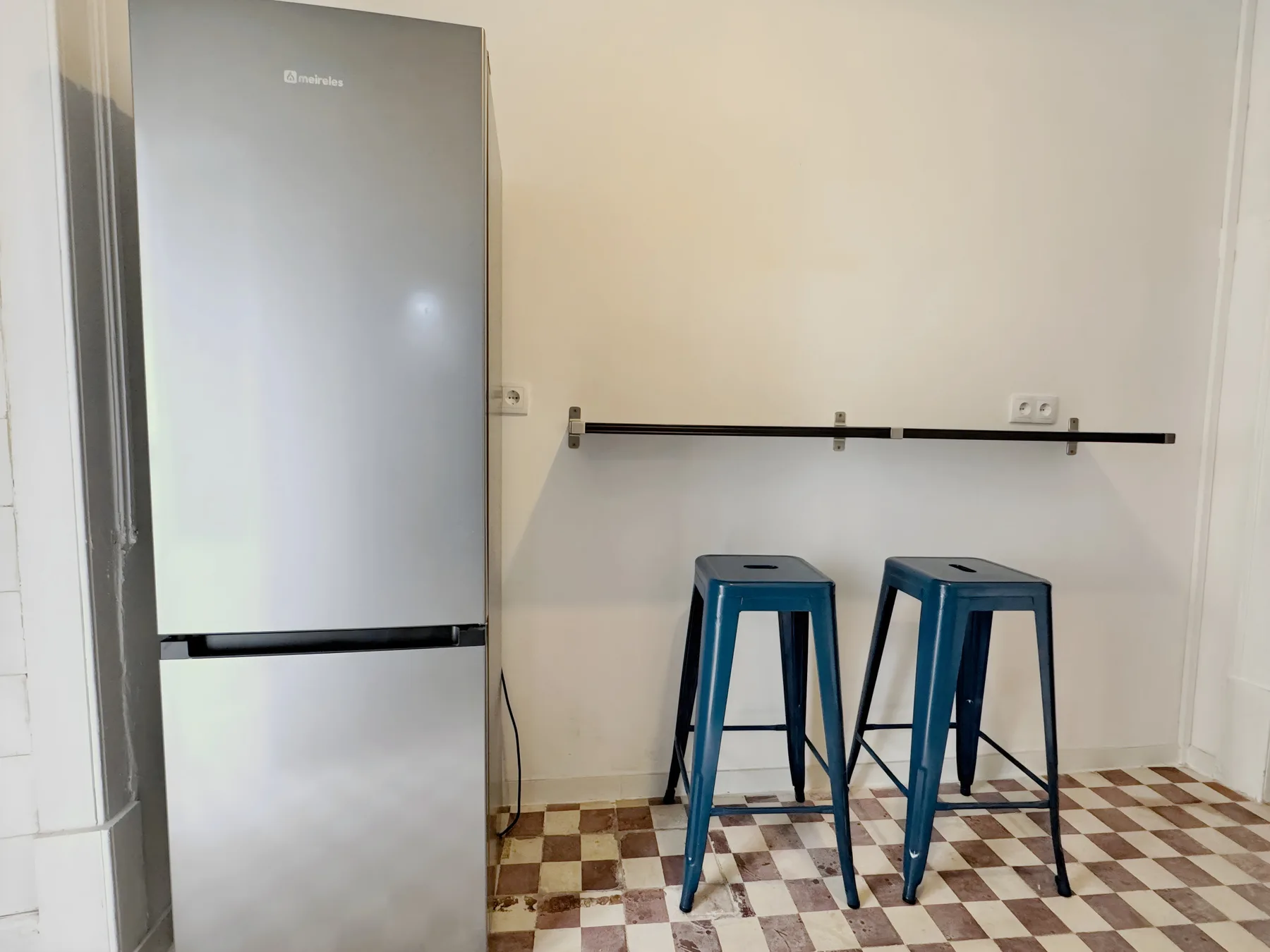 A kitchen counter area with two blue stools and a refrigerator.
