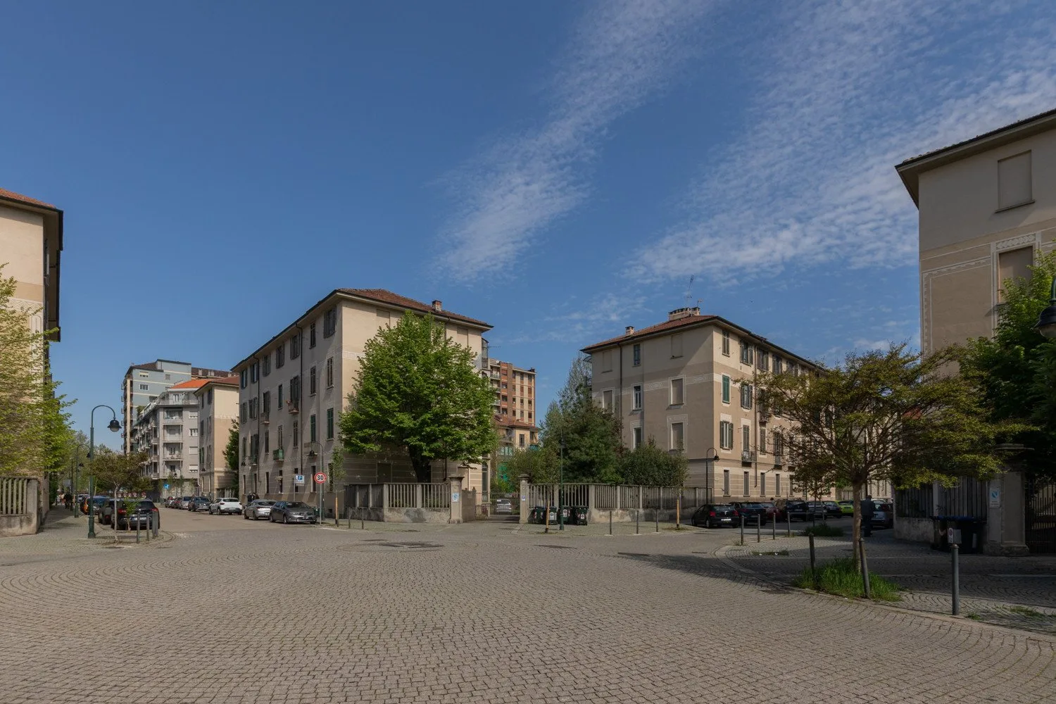 Una intersección urbana empedrada, bordeada de edificios residenciales y árboles.